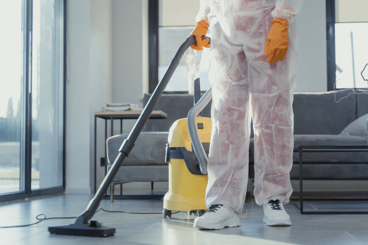 hero-img-01 A cleaner in protective coveralls and gloves vacuuming a modern living room.